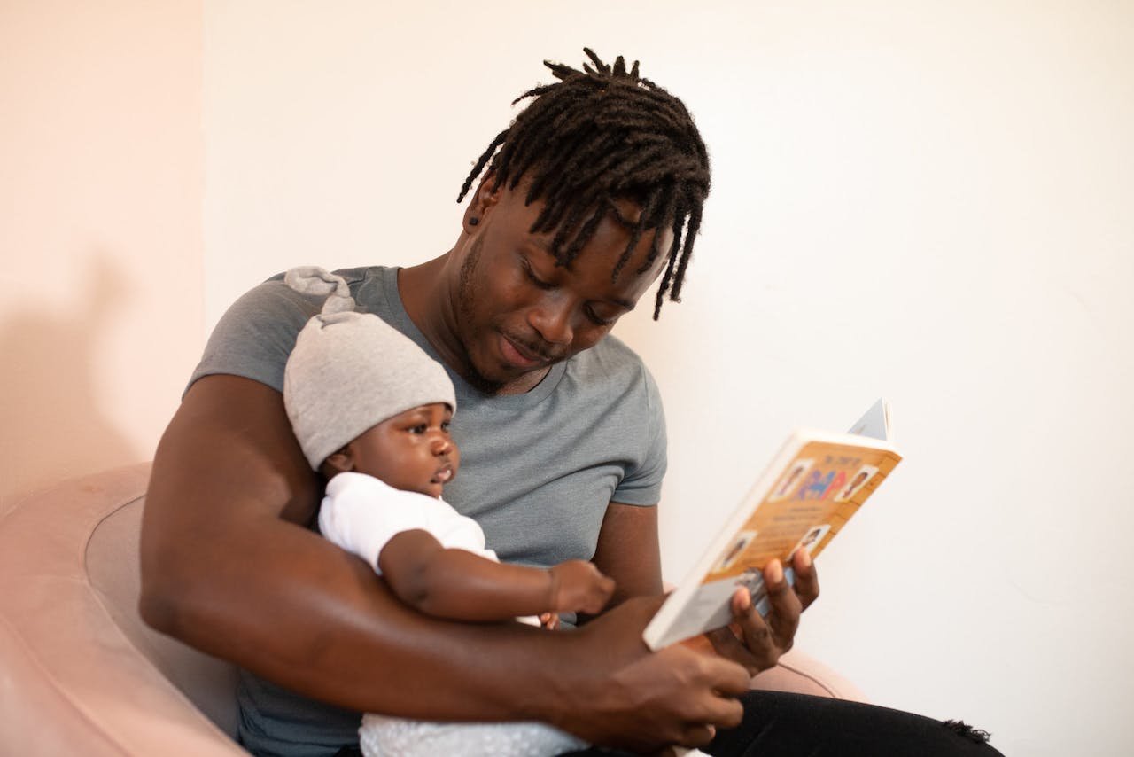 Black father reading his baby a book.